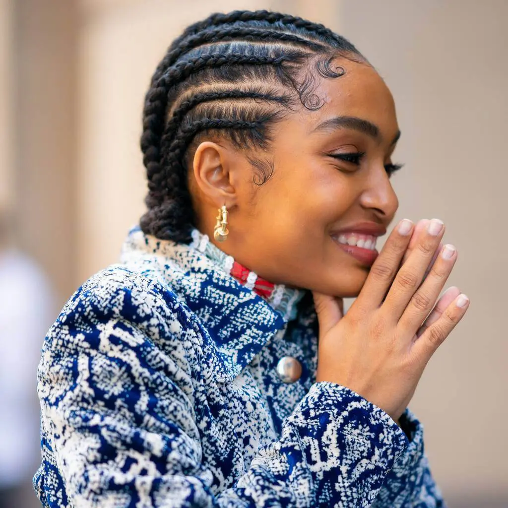 A woman with braids smiling and holding her hands together
