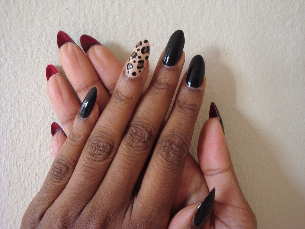 A woman's hands with black and red nail polish and a leopard print nail

