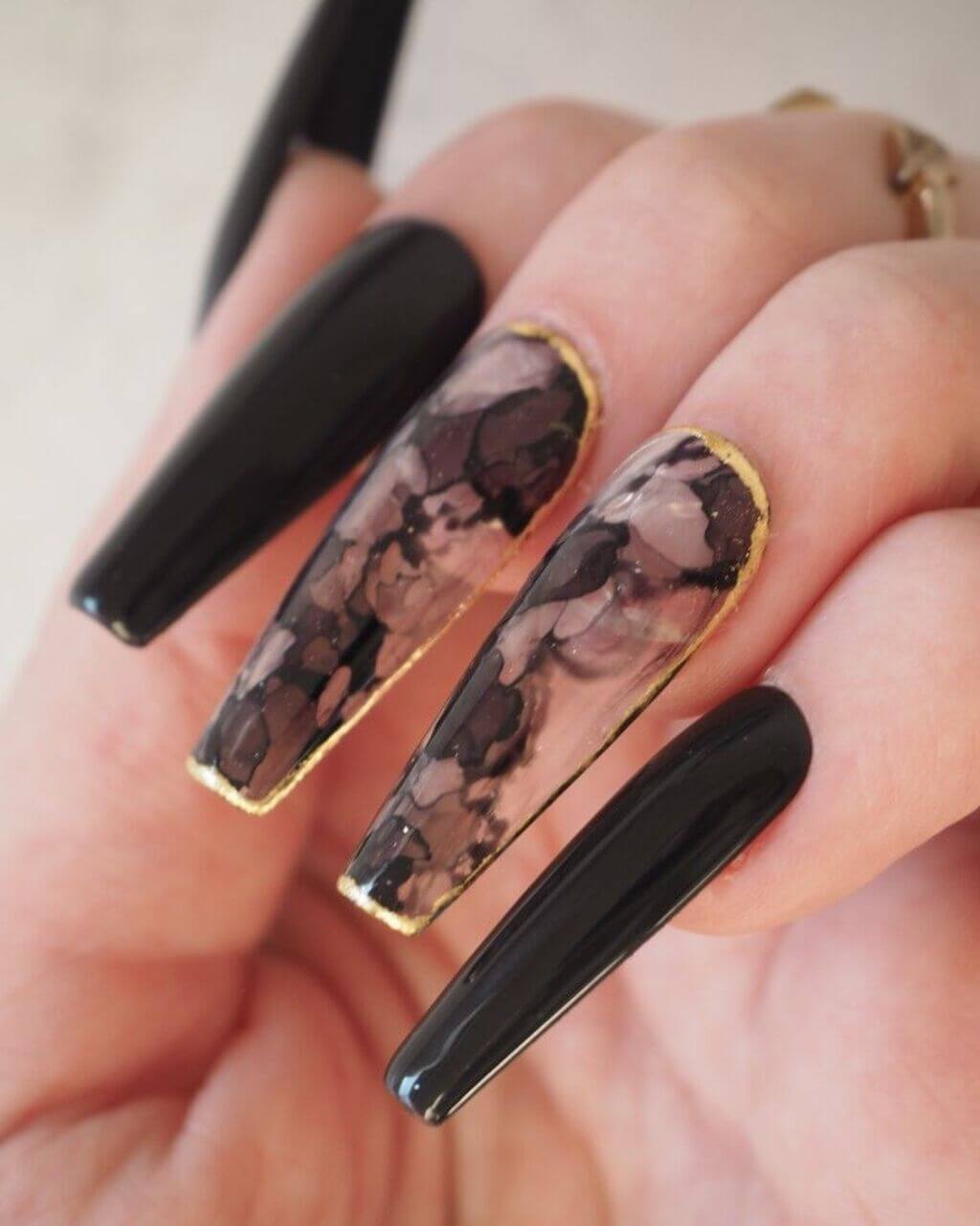 A woman's hand with a black and gold manicure with random design
