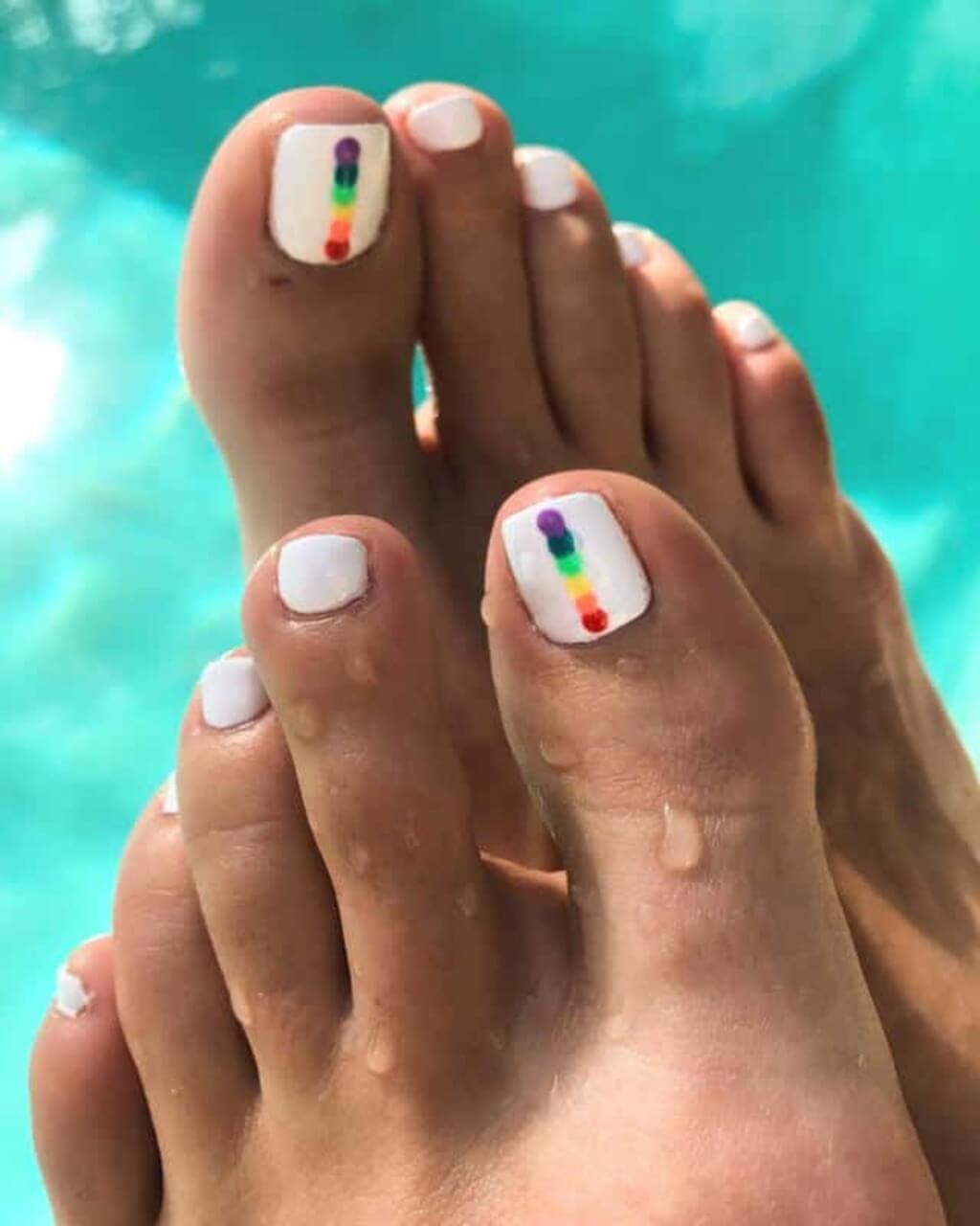 A women's feet with white and rainbow toenails
