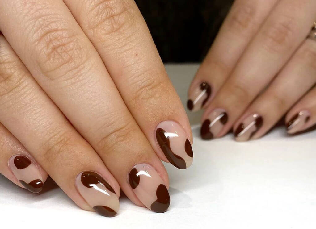 A woman's hands with brown and white nail polish
