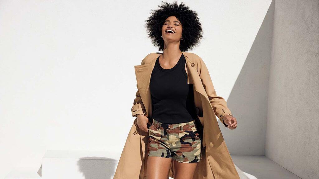 A woman in a trench coat and camo shorts
