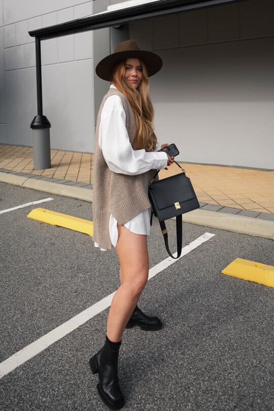 A woman walking across a parking lot holding a black purse
